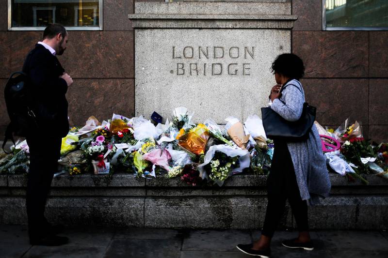 FILE - In this file photo dated Tuesday, June 6, 2017, people look at the floral tributes placed at London Bridge to commemorate the victims of Saturday's attack in London.  The inquest concluded Friday June 28, 2019,  into the van and knife attack, saying the victims of the London Bridge and Borough Market terror attacks on June 3, 2017, were unlawfully killed, and criticized the lack of barriers to protect pedestrians on London Bridge. (AP Photo/Markus Schreiber, FILE)