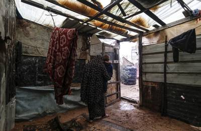 A Palestinian woman carries a child as she walks out of her family tent, made of tin and nylon sheets, on a rainy day in al-Amal (hope in Arabic) neighbourhood of Beit Lahia in the northern Gaza Strip.  AFP