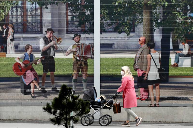 A woman passes an advertising photo-wall that shows traditional Bavarian musicians downtown in Munich, Germany. AP Photo