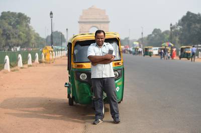 Indian auto rickshaw driver Vinod Kumar, 43, poses with his smartphone that he uses for a ride hailing app where customers can book his auto service, on a roadside near India Gate in New Delhi on November 9, 2018. (Photo by Money SHARMA / AFP)
