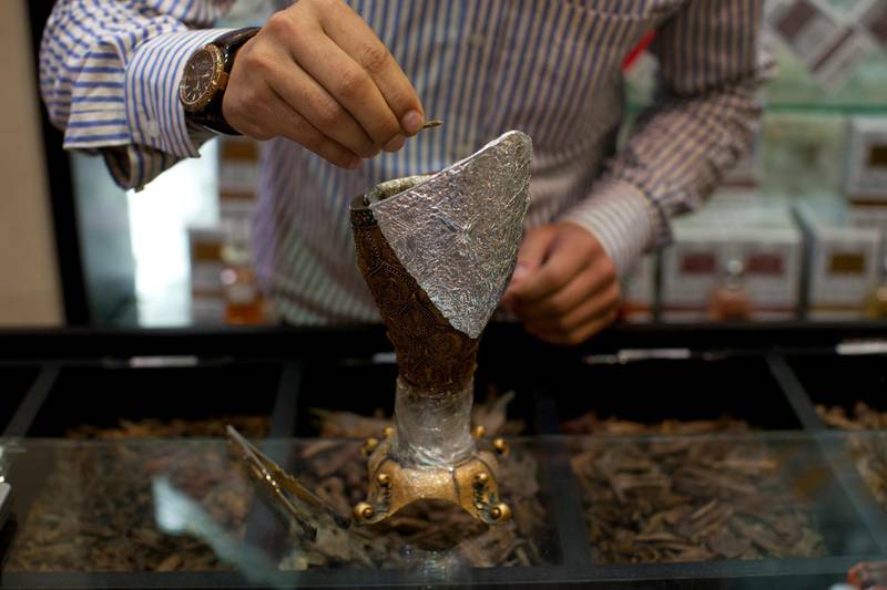 Dubai, United Arab Emirates - May 31 2012 - A sales clerk drops a piece of oud into an incense burner at Ibn Battuta mall. Shopkeepers are now only allowed to burn incense inside the store and are not allowed to lure in customers by burning bakhour outside their stores. (Razan Alzayani / The National)