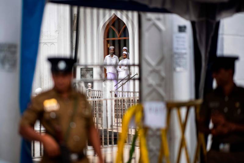Devotees look out from a mosque as security personnel stand guard during Friday noon prayer in Colombo. AFP