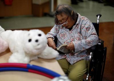 A resident reads a book during a session with 'AIBO'a pet dog robot and 'PARO' a robot seal at Shin-tomi nursing home in Tokyo, Japan, February 2, 2018. REUTERS/Kim Kyung-Hoon  SEARCH "KYUNG-HOON ROBOTS" FOR THIS STORY. SEARCH "WIDER IMAGE" FOR ALL STORIES.