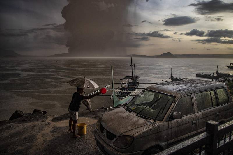 A resident splashes water on a vehicle covered in ash mixed with rainwater as Taal Volcano erupts. Getty Images