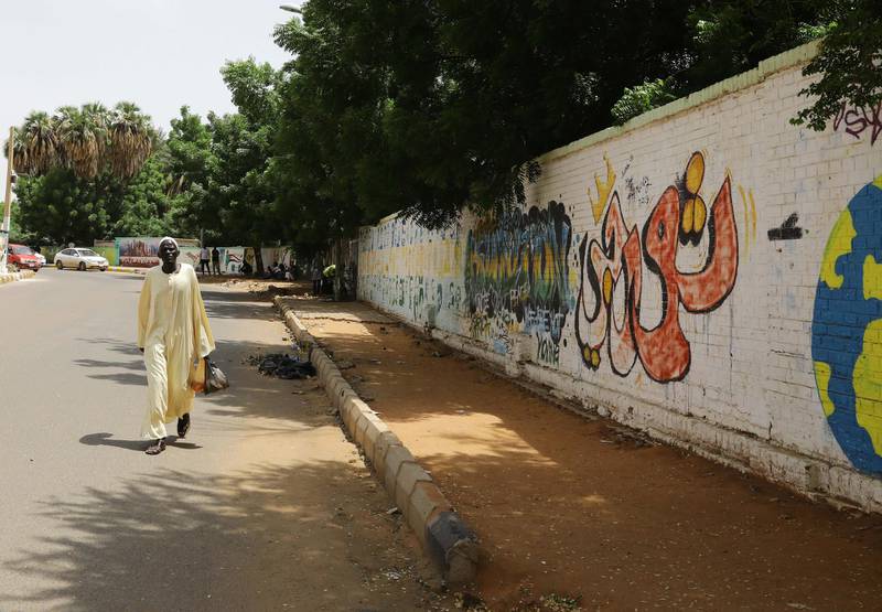 An elderly Sudanese man walks past fresh graffiti.