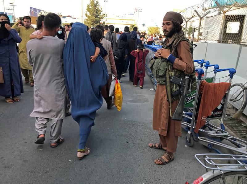 A member of the Taliban stands guard as people walk to the entrance gate of Hamid Karzai International Airport in Kabul on Sunday.