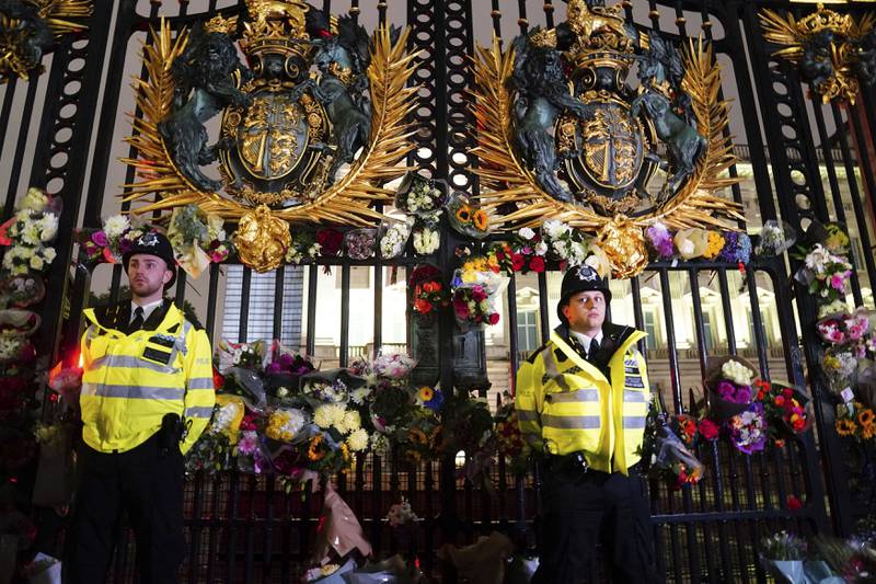 Police officers stand among floral tributes left outside Buckingham Palace. PA