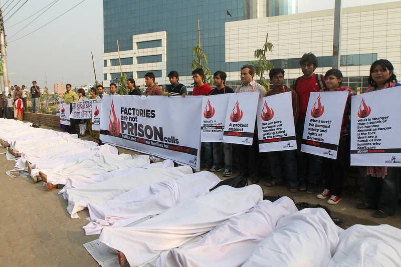 Bangladeshi activists pretend to be dead, wrapped in blankets,  following a deadly fire in a garment factory during a protest in Dhaka on November 29, 2012. Police arrested three managers of Tazreen Fashion factory hit by a fire, following charges that they stopped workers from leaving the burning plant when the fire alarm sounded, insisting that it was just a routine drill, referring to a weekend blaze at a local garment factory that left 110 people dead and more than 100 injured.  AFP PHOTO/STR (Photo by STR / AFP)
