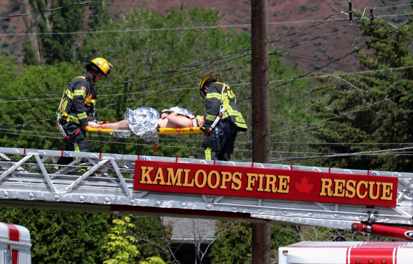 First responders carry an injured person on a stretcher across a fire truck ladder from a rooftop at the scene of a crash involving a Canadian Forces Snowbirds aircraft in Kamloops, British Columbia, Sunday, May 17, 2020. (Brendan Kergin/Castanet Kamloops/The Canadian Press via AP)