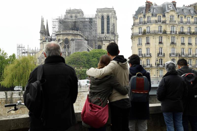 TOPSHOT - People hug while looking at Notre-Dame-de-Paris on April 16, 2019 in the aftermath of a fire that devastated the cathedral.
 Paris was struck in its very heart as flames devoured the roof of Notre-Dame, the medieval cathedral made famous by Victor Hugo, its two massive towers flanked with gargoyles instantly recognisable even by people who have never visited the city. / AFP / Bertrand GUAY
