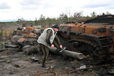 A man leans his foot on the barrel of a destroyed Russian tank while tying his shoelace, in Andriivka, Kyiv region. AFP