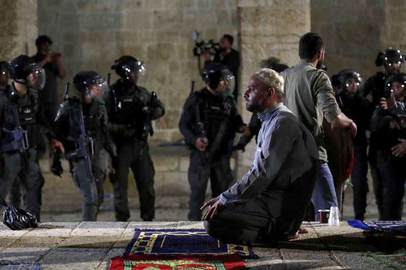 A Palestinian man prays as Israeli police gather during clashes at the Al Aqsa Mosque compound. Reuters