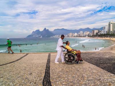 South America, Brazil, Rio de Janeiro, male nurse pushing someone in a wheelchair along the Ipanema Beach. Getty Images