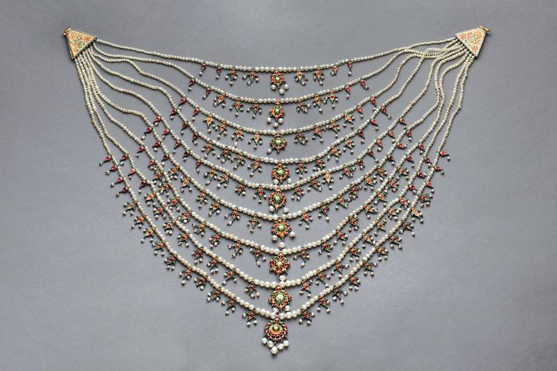 Antique necklace made from natural Gulf pearls with multi coloured enamel and white stonesc. 1880, IndiaH. 380mm;  W. 500mmZNM.2015.01813Zayed National Museum Description:A key object from the collection of Zayed National Museum, this antique pearl necklace in the Indian Satlada style was gifted to the renowned Egyptian singer Umm Kulthum by the late Sheikh Zayed bin Sultan Al Nahyan, Founding Father and first President of the United Arab Emirates. Known as ‘Kawkab Al Sharq’ — Star of the East, Umm Kulthum spent decades touring across the Arab world. Alongside her vocal talents, she was beloved for her charity work and her championing of Arab culture. Such a gift reflects the region’s long pearling history. The discovery of a natural pearl in a Neolithic house on Marawah Island, Abu Dhabi, provides strong evidence that pearls have been harvested and valued in the region for nearly 8,000 years. Treasured by the singer, the pearl necklace given to Umm Kulthum was handcrafted in India in the late 19th century. The Arabian Gulf was, at the time, the main supplier of pearls to the rest of the world mainly through India, meeting 80-90 per cent of global needs.  The necklace comprises 1,888 natural pearls arranged into nine rows, the centre of which has a pattern of four juxtaposed pearls followed by a small enameled pendant. The pearls decrease in size from the centre of the necklace to the tips of each strand. Additional pearls hang loosely from each red and green enameled pendant. To accommodate the curvature of the necklace, the number of pendants on each strand decreases towards the neckline. The largest pendant, located in the centre of the lowest string, has five large oval-shaped pearls hanging loosely below the necklace.