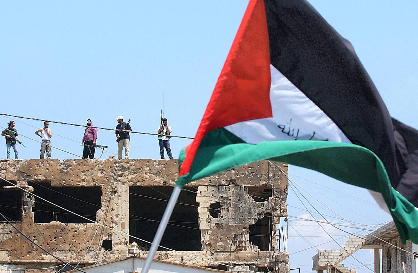 A Palestinian flag is waved during a rally to protest the Israeli incursion into Gaza, as armed Palestinian militants stand guard atop a damaged building, in the Burj-el-Barajneh Palestinian refugee camp, in the suburbs of Beirut, Lebanon, Friday, June 30, 2006. Following Friday prayers, Palestinians from different refugee camps in Lebanon staged sit-in protests condemning the Israeli incursion into Gaza and demanded world action to protect the Palestinians. (AP Photo/Jean Haddad)