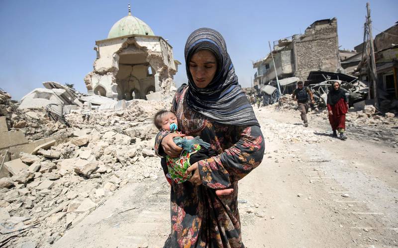 (FILES) In this file photo taken on July 05, 2017 An Iraqi woman, carrying an infant, walks by the destroyed Al-Nuri Mosque as she flees from the Old City of Mosul on July 5, 2017, during the Iraqi government forces' offensive to retake the city from Islamic State (IS) group fighters. Iraqi forces announced the "liberation" of the country's second city on July 10, 2017, after a bloody nine-month offensive to end the Islamic State (IS) group's three-year rule there. 
Scores of people are still displaced in and around Mosul as the city lies in ruins, one year after it was retaken from IS. 

 / AFP / AHMAD AL-RUBAYE
