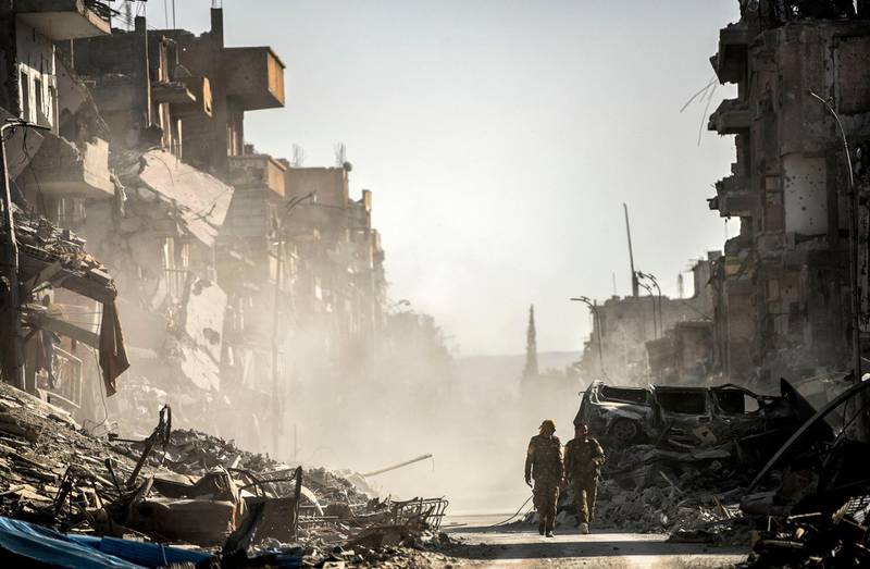 (FILES) This file photo taken on October 20, 2017 shows fighters of the Syrian Democratic Forces (SDF) walking down a street in Raqa past destroyed vehicles and heavily damaged buildings after a Kurdish-led force expelled Islamic State (IS) group fighters from the northern Syrian city, formerly their "capital".
2017 will be remembered as the year the Islamic State organisation's ultra-violent experiment in statehood was terminated but Iraq and Syria are left staring at ruined cities and daunting challenges. / AFP PHOTO / BULENT KILIC
