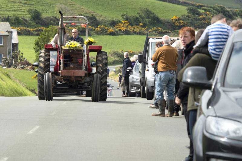 DOUGLAS, ISLE OF MAN - MAY 20: People line the street for Michael Quirk's funeral which is being lead by a man driving a tractor on May 20, 2020 in Douglas, Isle of Man. The Isle of Man began lifting COVID-19 lockdown restrictions on Friday 24th April with phase one, relaxing travel and exercise times, of a six phase plan. Two weeks later the chief minister, Howard Quayle, reopened non-essential retail shops plus lifestyle and tourism businesses - two further phases. Restaurants and cafes with outside dining will be able to open from June 1. The final phase will be reopening the island's borders, which closed on 27 March, and is still to come. This will be implemented on "clinical advice and dependent on the viral load of the UK" Mr Quayle said. (Photo by Andrew Barton/Getty Images)