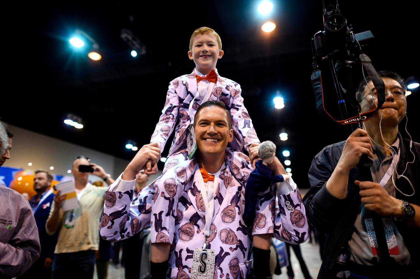 A shareholder and his son, both dressed in suits with pictures of Warren Buffett, CEO of Berkshire Hathaway, try to get a glimpse of Buffett as he arrives at the 2019 annual shareholders meeting in Omaha, Nebraska, May 4, 2019.  / AFP / Johannes EISELE
