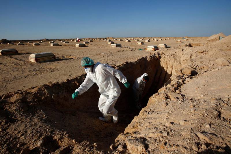 Members of the PMF, who volunteered to work in the cemetery, wearing a protective suit as he checks a grave before burial at new Wadi Al Salam cemetery. REUTERS