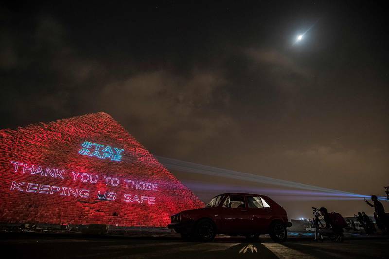 People take pictures of the Great pyramid of Kheops where a laser projection writes "Stay home, thanks to those keeping us safe".  AFP