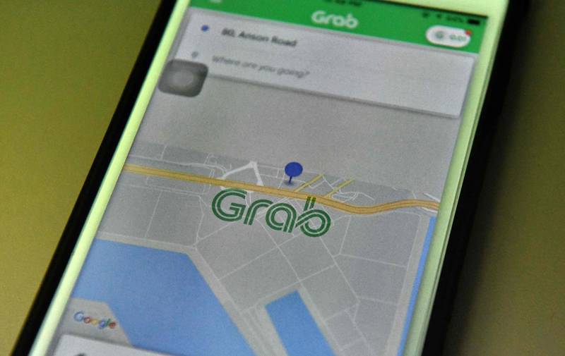 This photo illustration taken on March 26, 2018 shows the Grab booking application seen on a smart phone in Singapore. 
Singapore-based ride-hailing firm Grab announced on March 26 it has bought US rival Uber's business in Southeast Asia, ending a fierce battle for market share in the region. / AFP PHOTO / Roslan RAHMAN