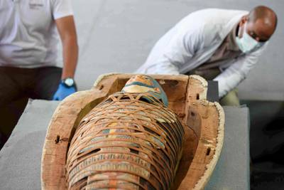 Archaeologists inspect a mummy, wrapped in a burial shroud adorned with brightly coloured hieroglyphics pictorials. AFP