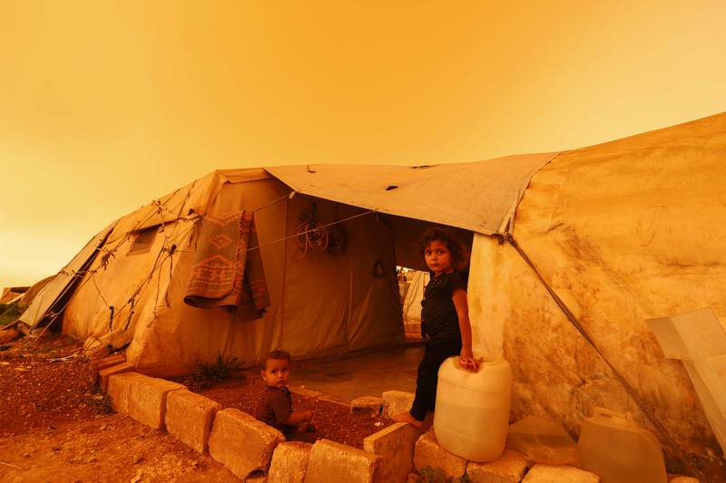 Displaced children sit next to their tent during the dust storm in Zardana.