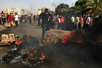 Sudanese protesters jump over a roadblock made of bricks and burning tyres as they rally on 60th Street in the capital, Khartoum.