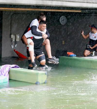 Japan's rugby team player Jiwon Koo, carries teammate James Moore in a flooded walkway at a stadium in Tokyo as the team practices ahead of their match against Scotland. AP