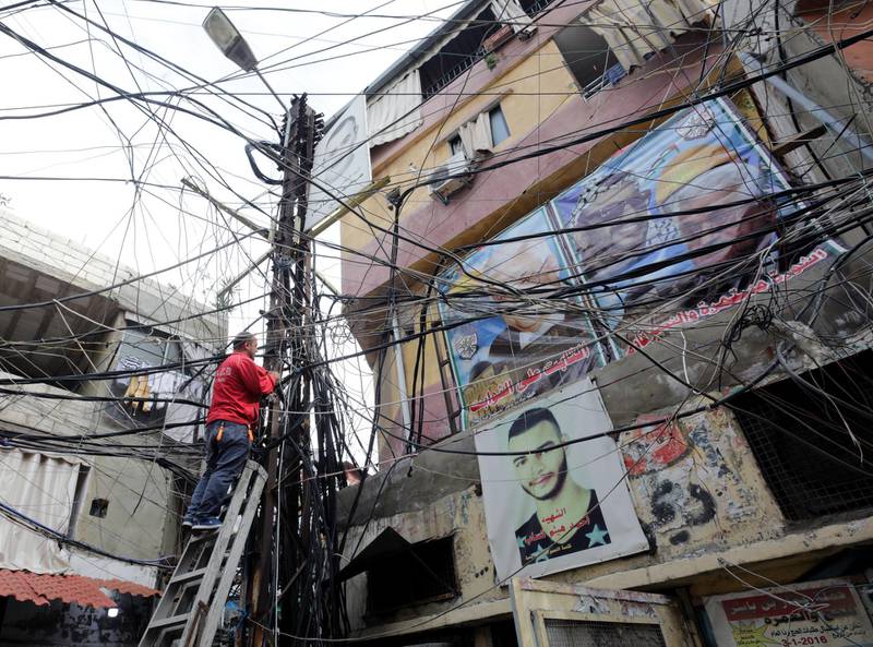 A picture taken on December 21, 2017 shows a man climbing a ladder to a pole where wires are  criss-crossing, next to posters of late Palestinian leader Yasser Arafat and president Mahmoud Abbas hung on a building in the Burj al-Barajneh camp, a southern suburb of the Lebanese capital Beirut. - More than 174,000 Palestinian refugees live in Lebanon, authorities announced on December 21, in the first-ever census of its kind for a country where demographics have long been a sensitive subject.
The census was carried out by the government's Lebanese-Palestinian Dialogue Committee in 12 Palestinian camps as well as 156 informal "gatherings" across the country. (Photo by ANWAR AMRO / AFP)
