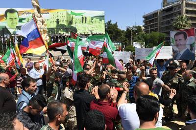 Syrians wave the Russian and Iranian flags and carry portraits of President Bashar al-Assad as they gather in Aleppo's Saadallah al-Jabiri square on April 14, 2018, to condemn the strikes carried out by the United States, Britain and France against the Syrian regime. / AFP PHOTO / George OURFALIAN