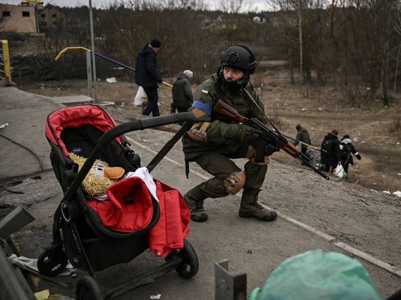 A Ukrainian soldier takes cover as people flee Irpin. AFP