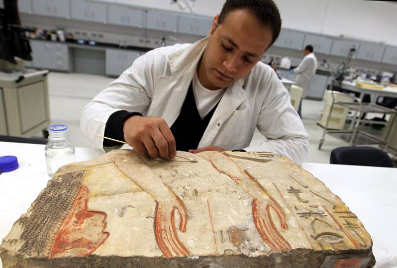 An Egyptian archeological restoration technician works on a limestone board marked with hieroglyphics. Khaled Elfiqi / EPA