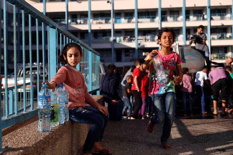 Palestinian girls who fled home due to Israeli air and artillery strikes, wait to fill bottles with water at a school hosting refugees in Gaza city. AFP