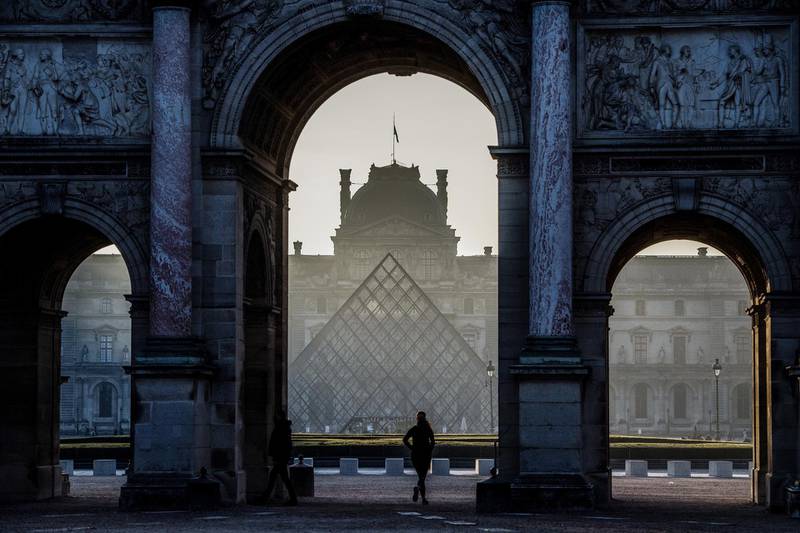 A woman runs under the Arc de Triomphe du Carrousel by the Louvre museum pyramid in the morning haze at dawn in Paris on March 22, 2019. - Chinese born US architect Ieoh Ming Pei's pyramid celebrates its 30th anniversary this month. (Photo by Christophe ARCHAMBAULT / AFP) / RESTRICTED TO EDITORIAL USE - MANDATORY MENTION OF THE ARCHITECT UPON PUBLICATION - TO ILLUSTRATE THE EVENT AS SPECIFIED IN THE CAPTION
