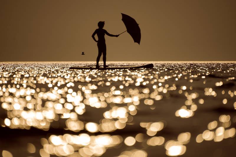 A woman steers her stand-up paddle board using an umbrella as a sail at Ladoga lake near the city of Olonets,  Russia. AP Photo