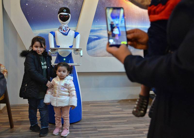 Children pose for a picture next to a robot waiter at the "White Fox" restaurant in the eastern part (left bank of the Tigris river) of Iraq's northern city of Mosul, on November 17, 2021. AFP