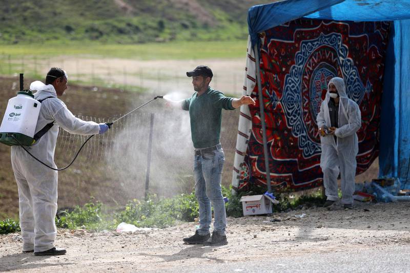 An employee of the Palestinian health ministry sprays disinfectant on a worker crossing back from Israel at the checkpoint of Tarqumiya, near the West Bank town of Hebron.  EPA
