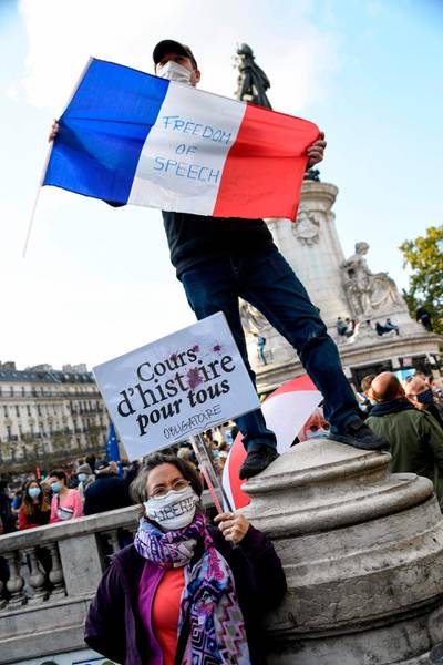 A woman holds a placard reading 'History course for eveyone' and a man holds a French flag on Place de la Republique in Paris. AFP