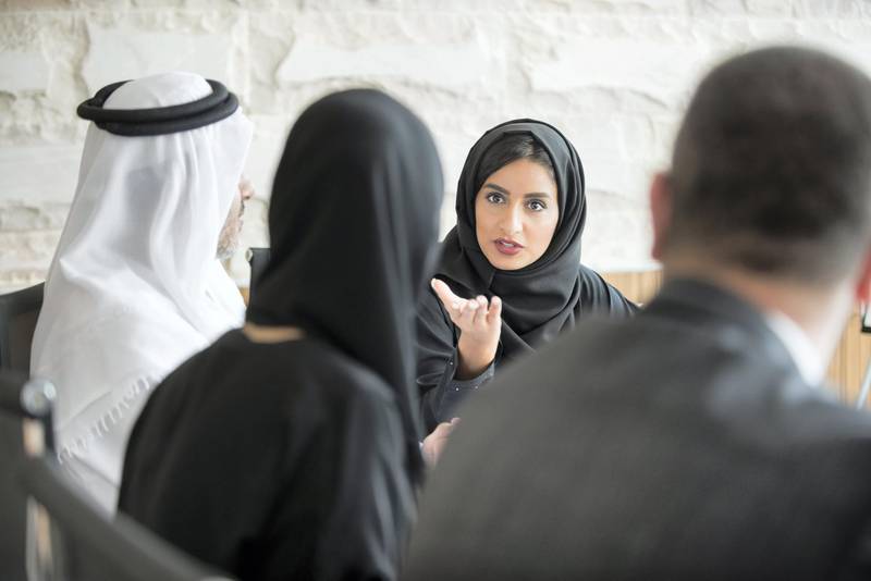 A photo of young and confident Arab businesswoman discussing in a meeting. Emirati woman wearing traditional abaya. Middle Eastern professional female is gesturing towards colleague while sitting in board room meeting.