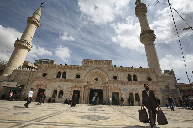 A man carrying his shopping bags walks ijn front of a mosque, ahead of the Muslim holy month of Ramadan, during the novel coronavirus pandemic crisis in the Jordanian capital Amman, on April 23, 2020. (Photo by Khalil MAZRAAWI / AFP)