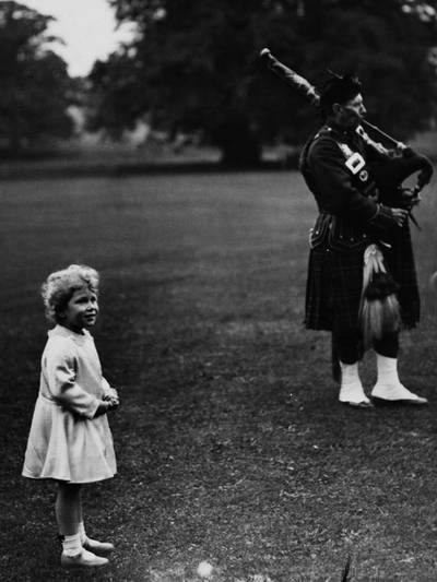 Princess Elizabeth (later Queen Elizabeth II) watches members of a pipe band play in the grounds of Glamis Castle near Forfar in Scotland in September 1929. (Photo by Topical Press Agency/Getty Images)