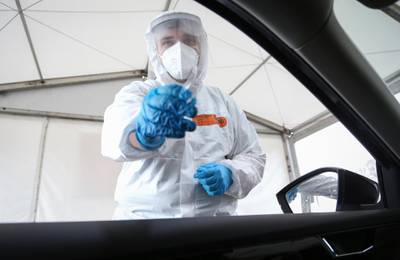 A drive-In testing station employee stands next to an open car window to take a nasal swab in Osnabrueck, Germany. AP Photo