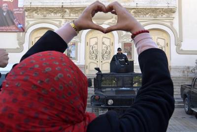 A Tunisian woman makes a heart sign as she stands in front of security forces guarding the area during a rally marking the ninth anniversary of the 2011 uprising on Habib Bourguiba Avenue in central Tunis on January 14, 2020. AFP