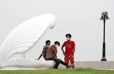 Three people wearing face masks sit in a giant oyster shell on the coast of Fujairah. Chris Whiteoak / The National