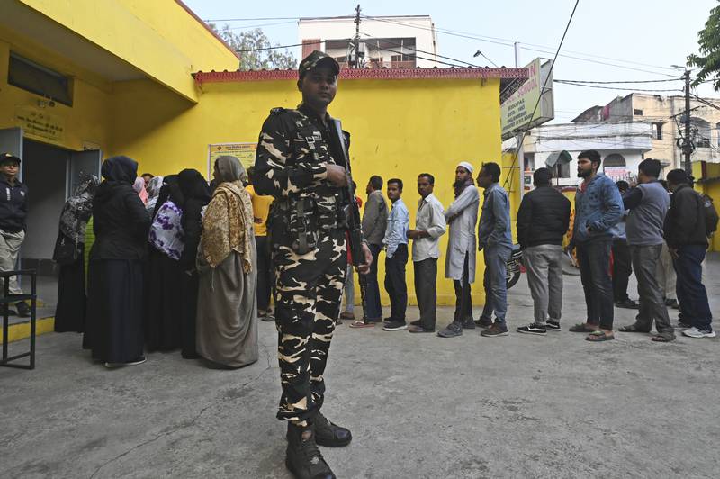 A security officer stands guard as people wait in a queue to cast their their votes for the state elections in Bhopal, Madhya Pradesh. AP Photo