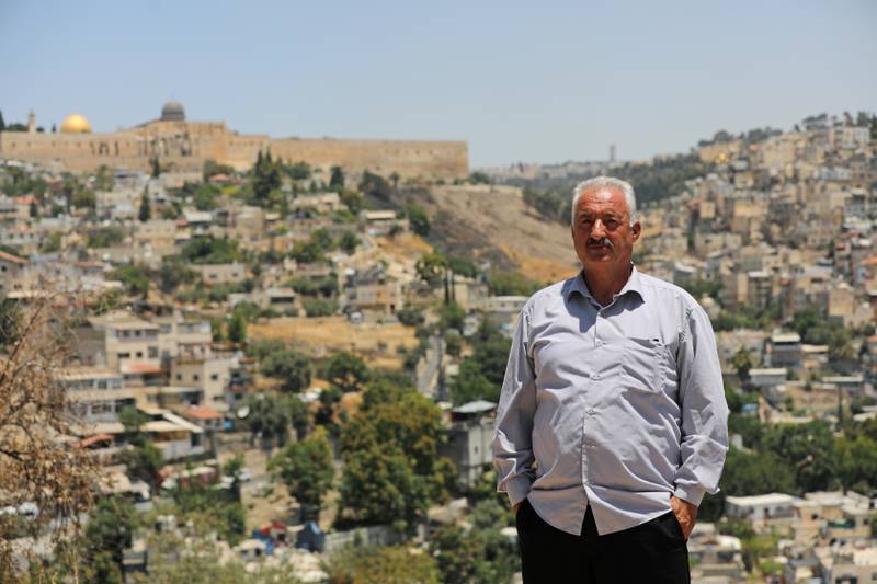 Fakhri Abu Diab, a Palestinian resident of the al-Bustan neighbourhood in Silwan, poses for a picture as part of his neighbourhood is seen behind him in East Jerusalem.