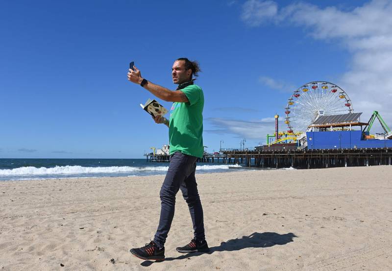 This picture taken on March 23, 2020 shows Adam Duford, owner of Surf City Tours, describing iconic sites in Santa Monica, California as part of a "virtual tour" via his Instagram feed, as the COVID-19 novel coronavirus situation forced his normal tour bus business to come to a halt.  / AFP / Robyn Beck
