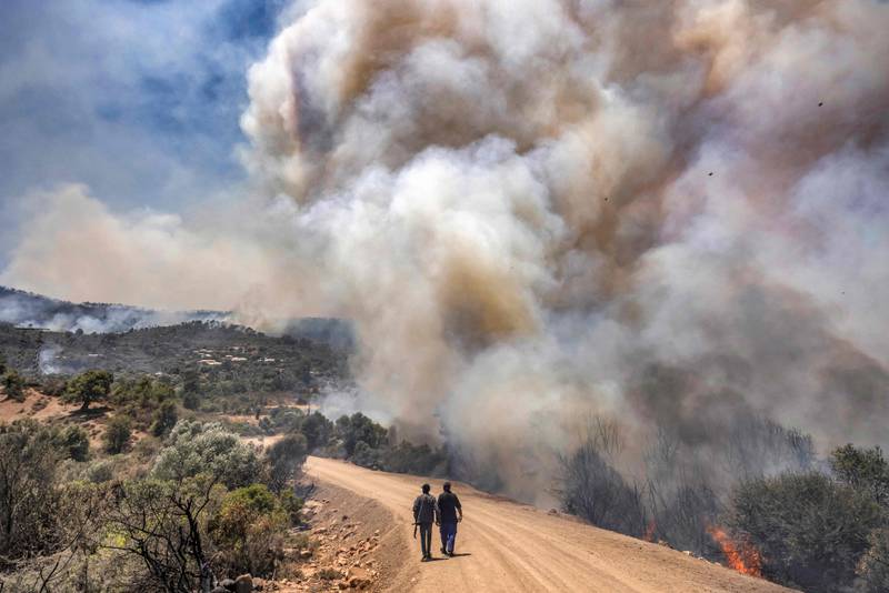 Men walk along a dirt road as a forest fire rages in Morocco's northern region of Ksar Sghir. AFP